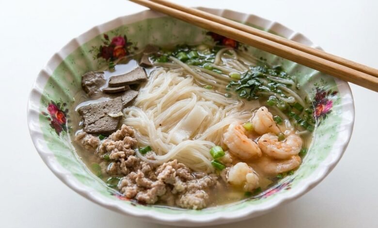 Overhead view of a bowl of Cambodian Phnom Penh noodle soup with pork, shrimp, and herbs.